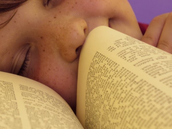 A child closes their eyes and sniffs the page of a book, smiling. (Decorative image.)