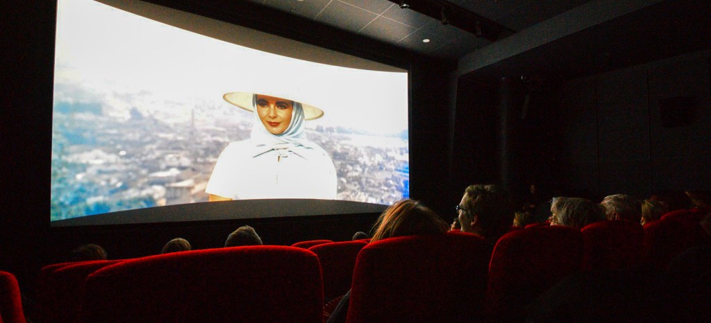 On screen in a movie theater, Elizabeth Taylor reveals her identity to the audience at the end of the film.
