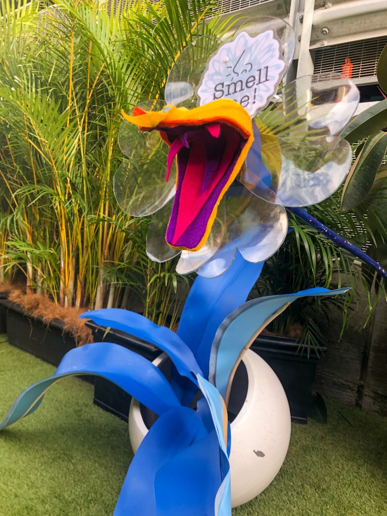 An alien orchid, fangs and tongue out, draws audiences near with its sweet smell.