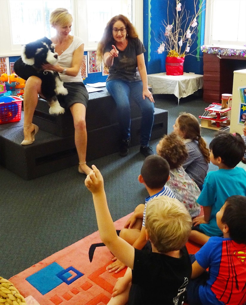 Pup, Emma, and Tammy sit in front of the children. A child raises their hand and Tammy calls on them.