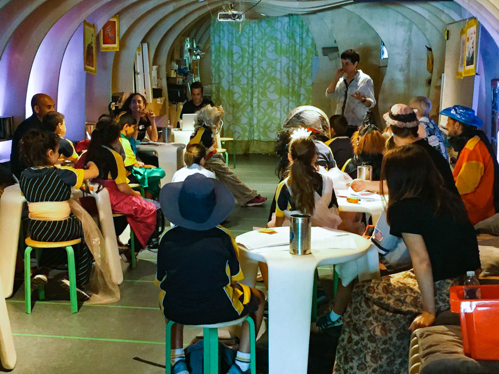 The "Scented Storytelling" workshop taking place in the Sydney Story Factory between the ribs of a whale. Tammy gestures and speaks while children and their parents look on in costume.